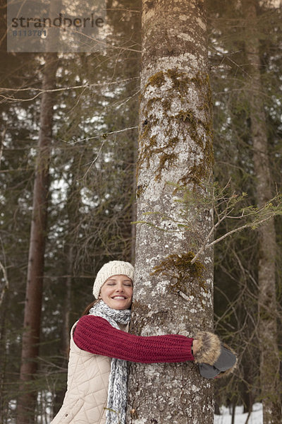 Glückliche Frau umarmt Baumstamm im Wald
