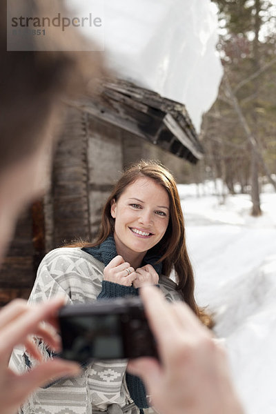 Mann fotografiert lächelnde Frau im Schnee außerhalb der Kabine