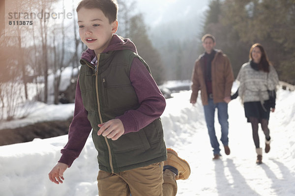 Eltern beobachten Jungen beim Laufen in der verschneiten Gasse