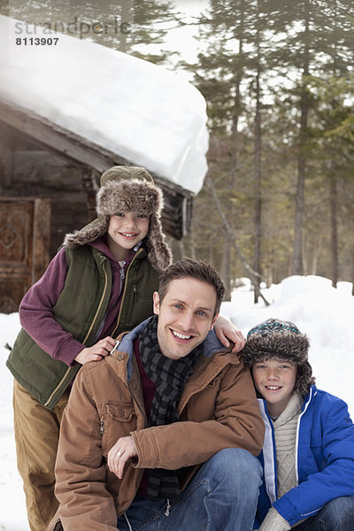 Porträt des lächelnden Vaters und der Söhne im Schnee vor der Hütte