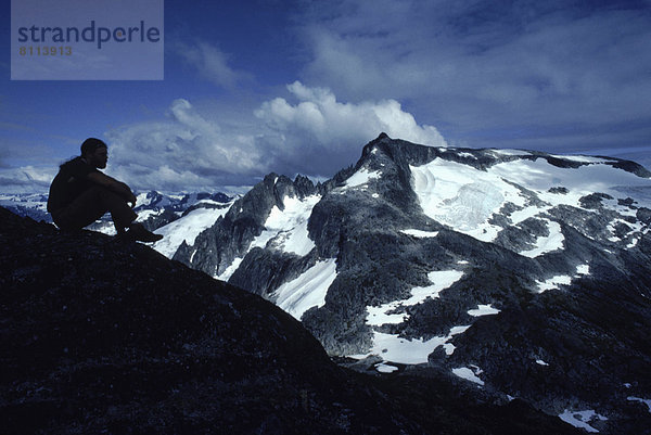 Vereinigte Staaten von Amerika  USA  hoch  oben  Außenaufnahme  sitzend  Einzelperson  eine Person  Berg  Farbaufnahme  Farbe  Tag  sehen  Wolke  Ruhe  Silhouette  Himmel  Hügel  Einsamkeit  Querformat  rauh  Fotografie  Seitenansicht  Freundlichkeit  nur ein Mann  Alaska  freie Natur  Hang  Schnee