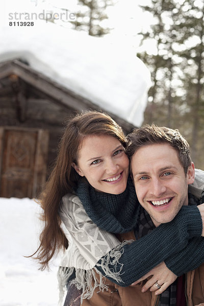 Portrait eines glücklichen Paares  das sich im Schnee außerhalb der Kabine umarmt.