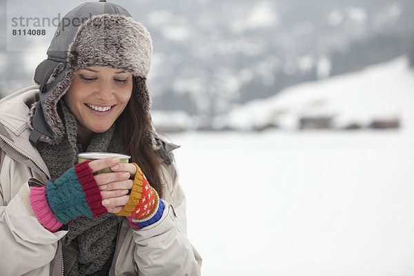 Lächelnde Frau trinkt Kaffee im Schnee