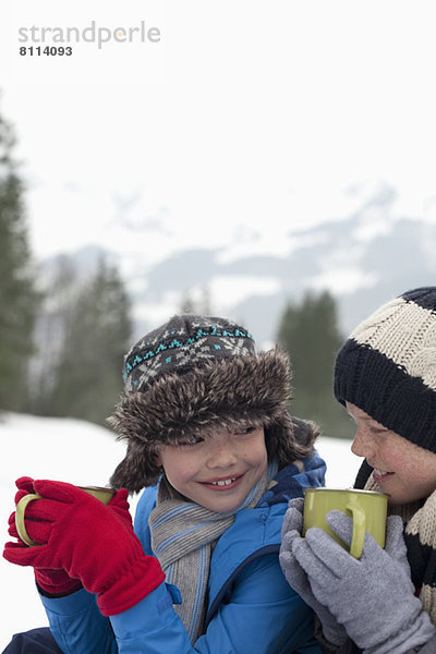 Nahaufnahme von fröhlichen Jungen beim Trinken von heißer Schokolade im Schneefeld