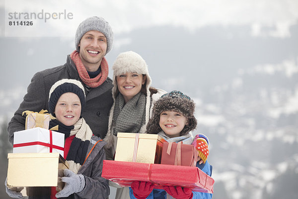 Porträt einer glücklichen Familie mit Weihnachtsgeschenken im Schnee