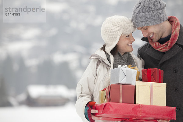 Glückliches Paar mit Weihnachtsgeschenken im Schnee