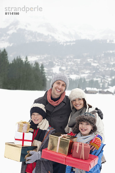 Porträt einer glücklichen Familie mit Weihnachtsgeschenken im Schneefeld