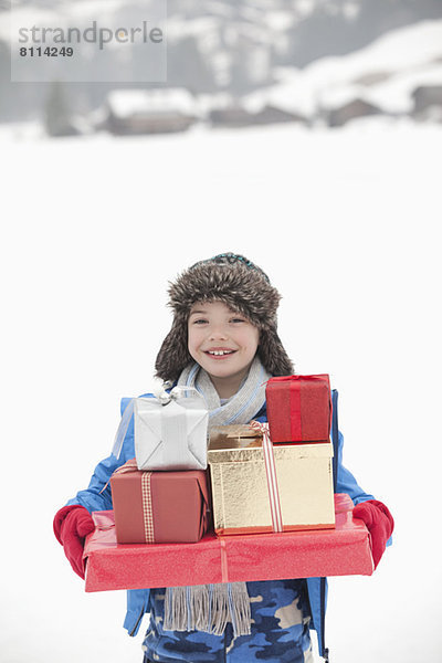 Porträt eines lächelnden Jungen mit einem Stapel Weihnachtsgeschenke im Schnee