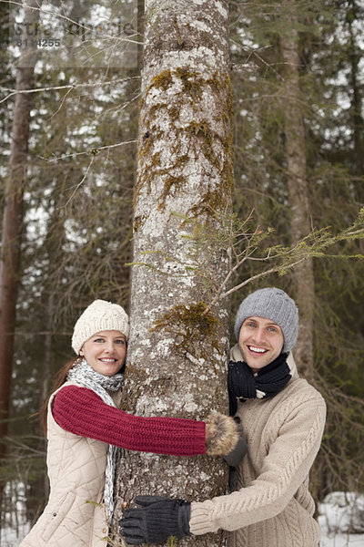 Porträt eines glücklichen Paares  das den Baumstamm im Wald umarmt.
