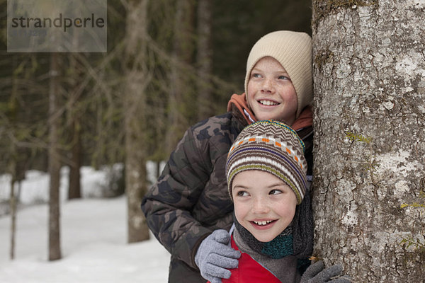Glückliche Jungen lehnen sich in verschneiten Wäldern an den Baumstamm.