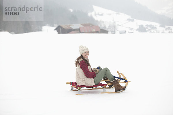 Porträt einer lächelnden Frau beim Rodeln im Schneefeld