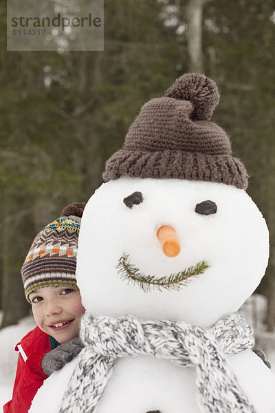Porträt des lächelnden Jungen hinter Schneemann mit Strumpfmütze