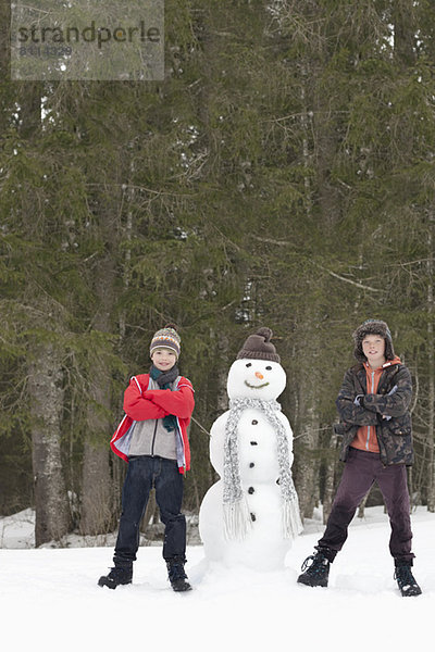 Porträt der selbstbewussten Jungen neben dem Schneemann im Wald