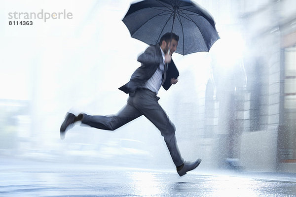 Geschäftsmann mit Regenschirm in der verregneten Straße