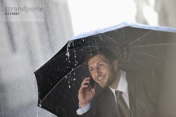 Geschäftsmann im Gespräch mit dem Handy unter dem Regenschirm