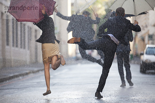 Geschäftsleute mit Regenschirmen tanzen im Regen