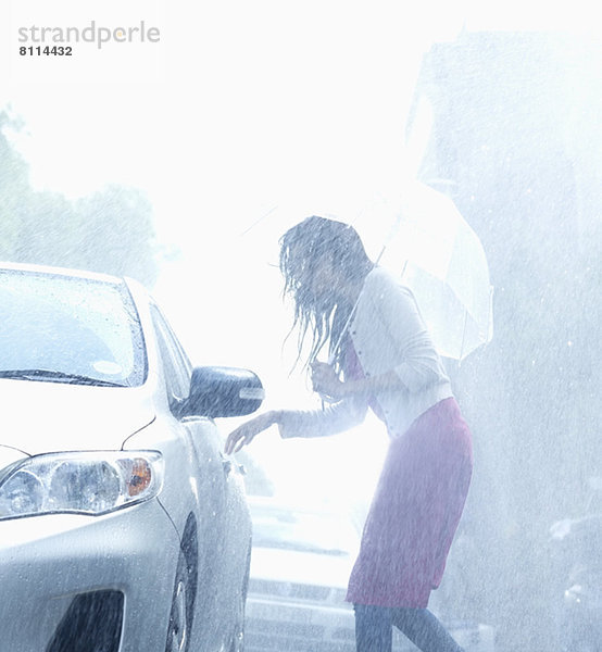 Frau mit Regenschirm für Autotürgriff im Regen