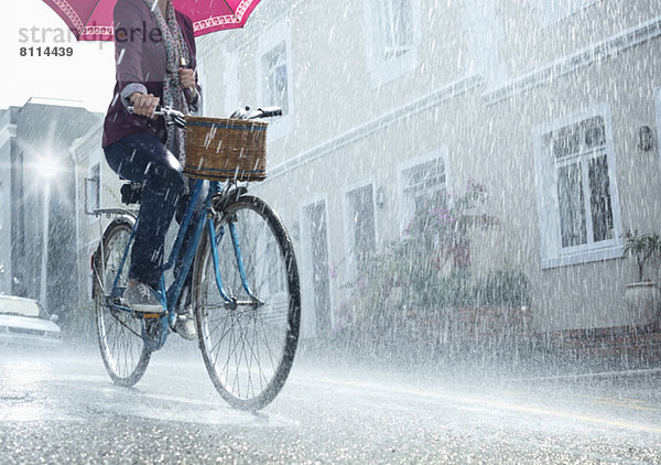 Fahrradfrau mit Regenschirm in verregneter Straße