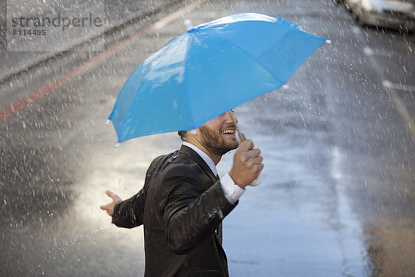 Geschäftsmann mit winzigem Regenschirm  der im Regen läuft.