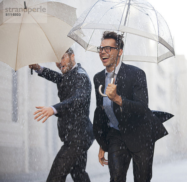 Glückliche Geschäftsleute mit Regenschirmen  die im Regen spazieren gehen