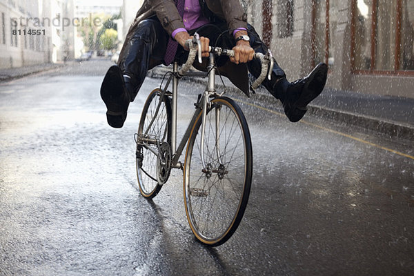 Geschäftsmann Fahrrad fahren mit Füßen im Regen