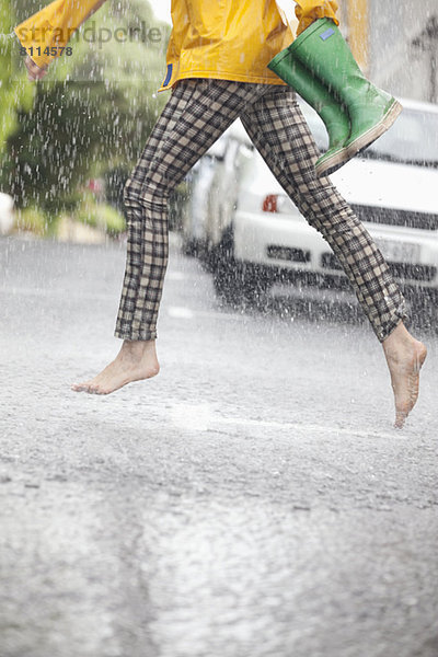 Barfüßige Frau  die im Regen über die Straße rennt.