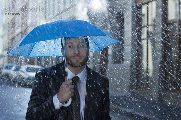 Portrait eines Geschäftsmannes mit winzigem Regenschirm