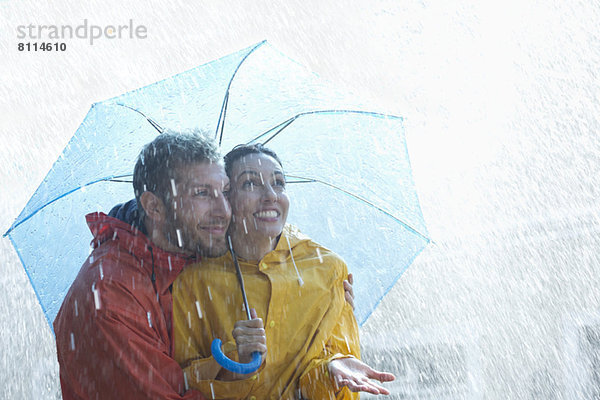 Glückliches Paar unter Schirm im Regen