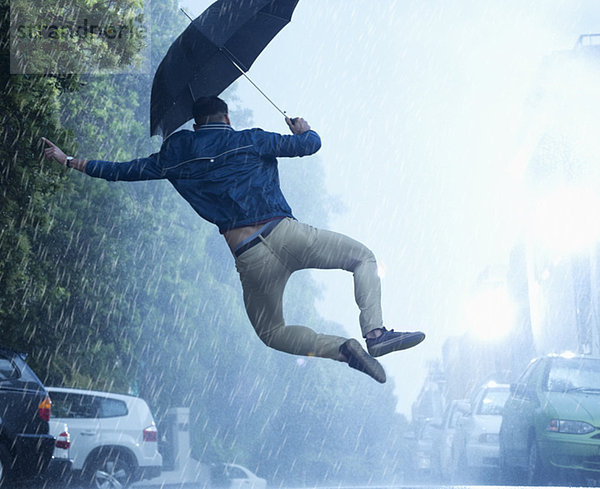 Mann mit Regenschirm springt im Regen