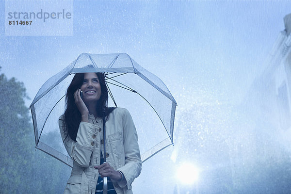 Geschäftsfrau beim Telefonieren unter dem Schirm im Regen