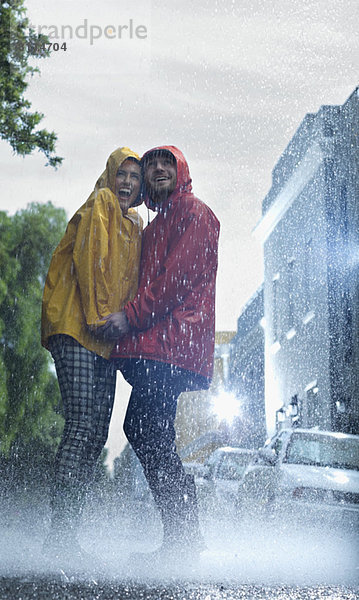 Glückliches Paar in Regenmänteln  das im Regen Händchen hält.