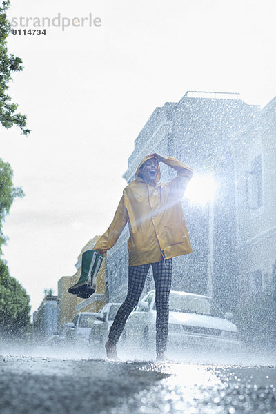 Frau im Regenmantel mit Gummistiefeln und barfuß gehen im Regen
