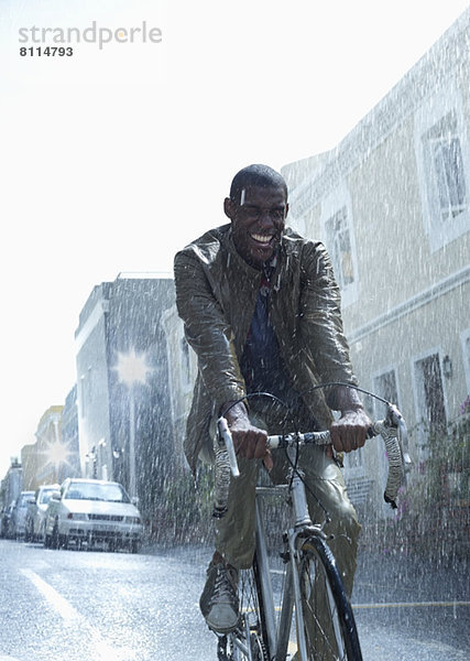Glücklicher Geschäftsmann beim Fahrradfahren im Regen