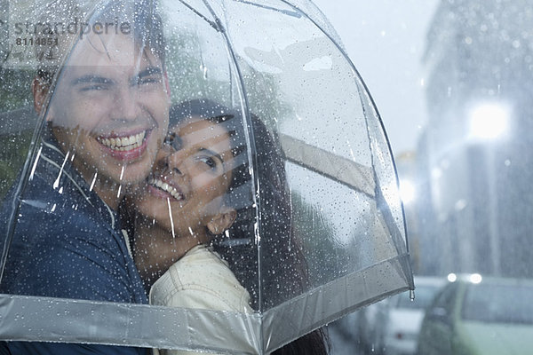 Glückliches Paar  das sich unter dem Regenschirm umarmt.