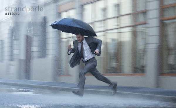 Geschäftsmann mit Regenschirm  der über die regnerische Straße läuft