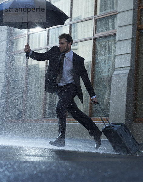 Geschäftsmann mit Koffer und Regenschirm über die regnerische Straße