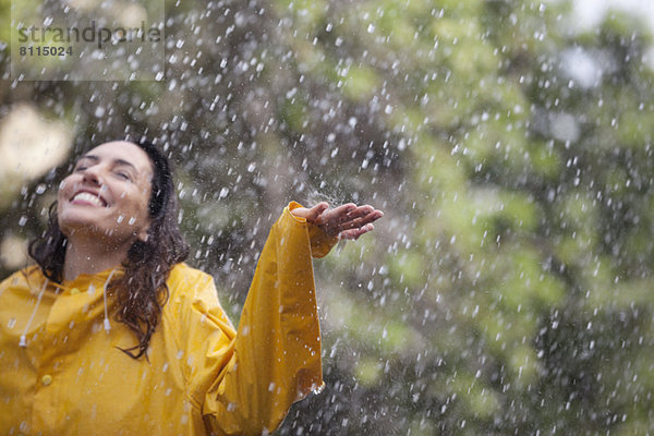 Glückliche Frau  die mit ausgestreckten Armen im Regen steht.