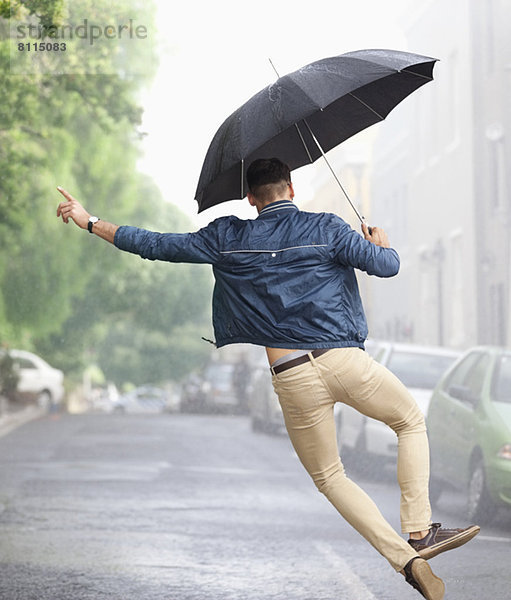 Mann tanzt mit Regenschirm in der verregneten Straße