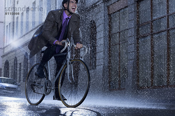 Enthusiastischer Geschäftsmann auf dem Fahrrad in der verregneten Straße