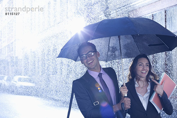 Glücklicher Geschäftsmann und Geschäftsfrau  die im Regen unter einem Regenschirm spazieren gehen.