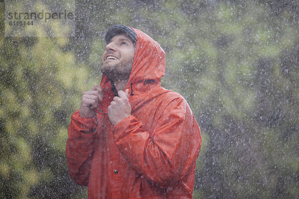 Lächelnder Mann mit Regenmantel schaut auf den Regen.
