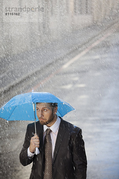 Geschäftsmann unter winzigem Regenschirm in verregneter Straße