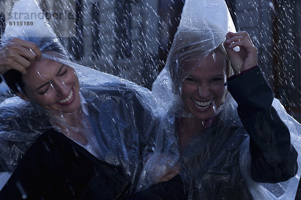 Lachende Geschäftsfrauen mit Ponchos im Regen