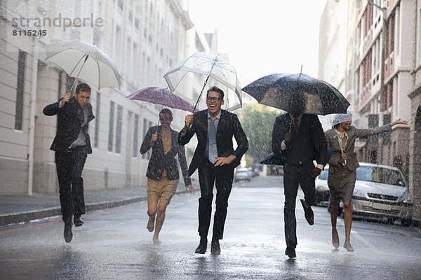 Geschäftsleute mit Regenschirmen in verregneter Straße