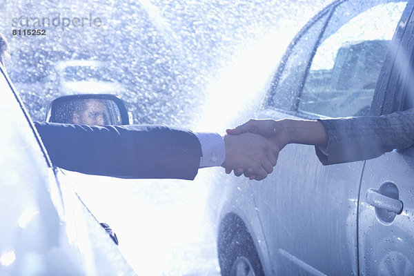 Geschäftsmann und Geschäftsfrau beim Händeschütteln von Autos bei Regen