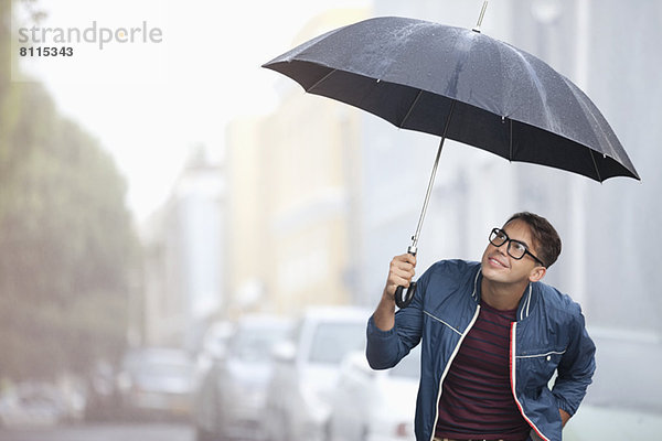 Mann mit Regenschirm schaut auf den Regen auf der Straße