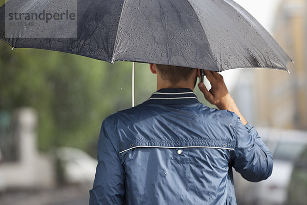Mann spricht auf dem Handy unter dem Schirm im Regen