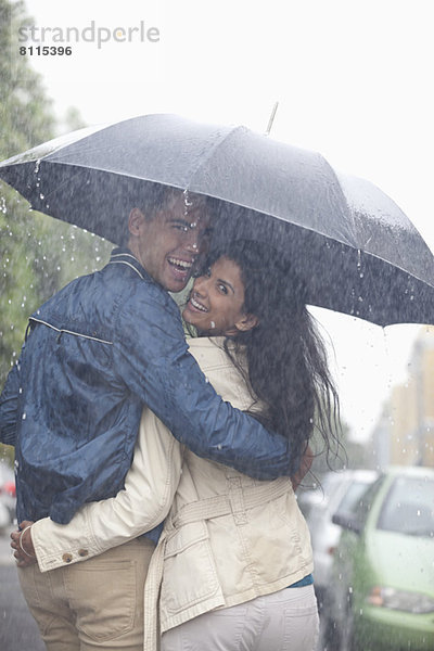 Porträt eines glücklichen Paares  das sich unter dem Regenschirm umarmt.