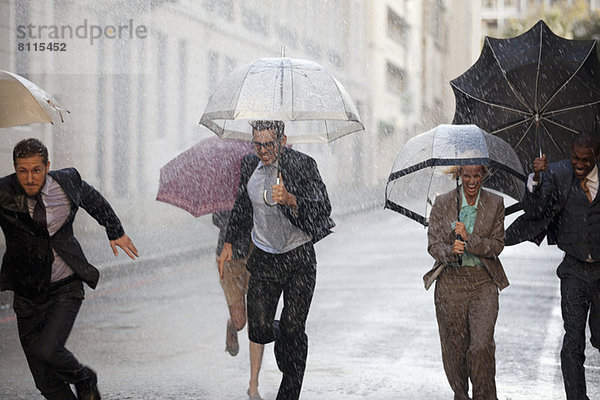 Begeisterte Geschäftsleute mit Regenschirmen in verregneter Straße
