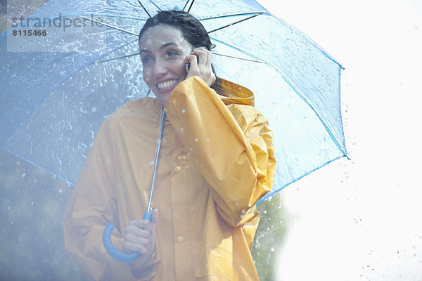 Fröhliche Frau beim Telefonieren unter dem Regenschirm